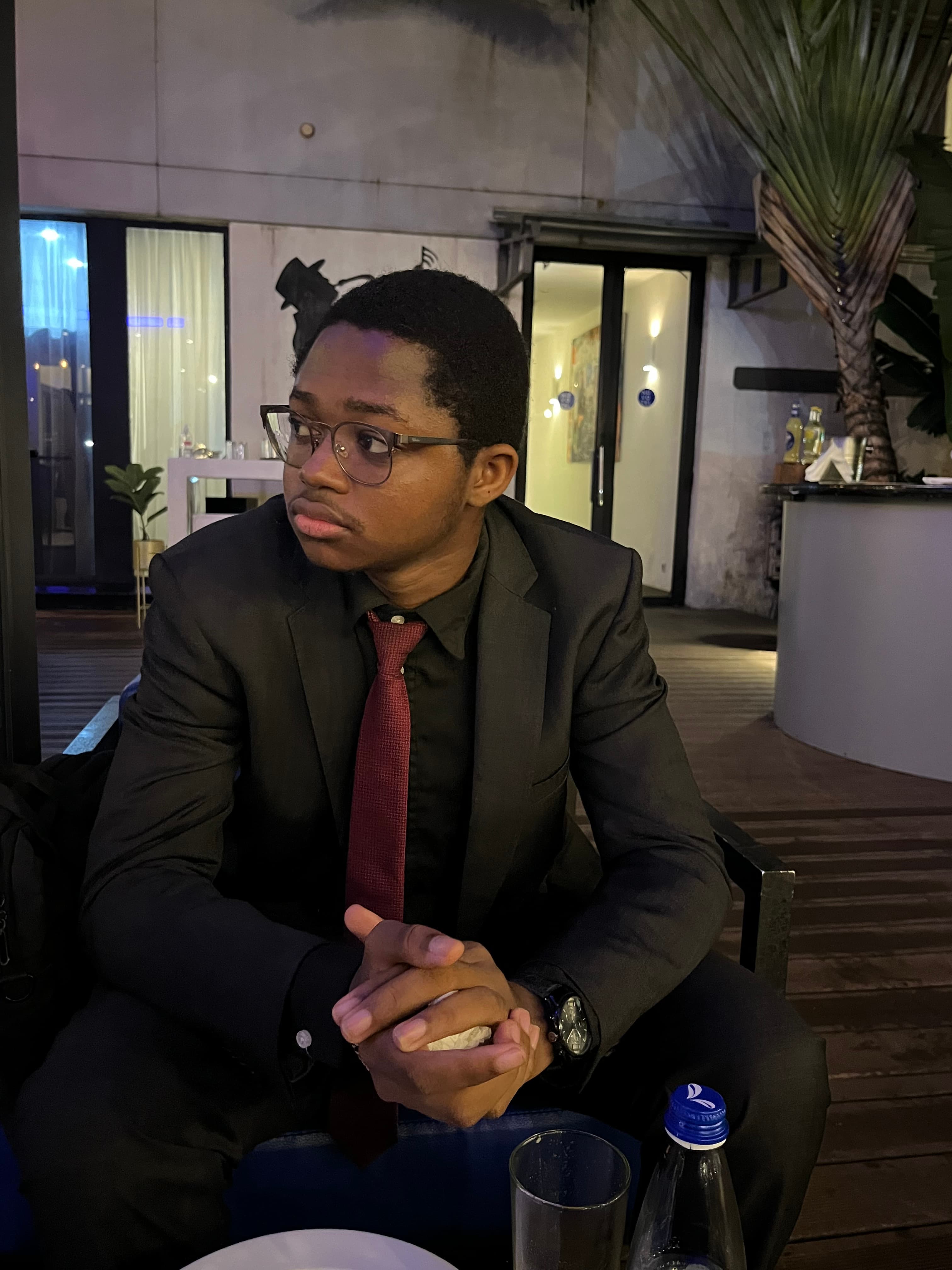 Kevin Zié Yeo assis en costume noir et cravate rouge lors d’une soirée.